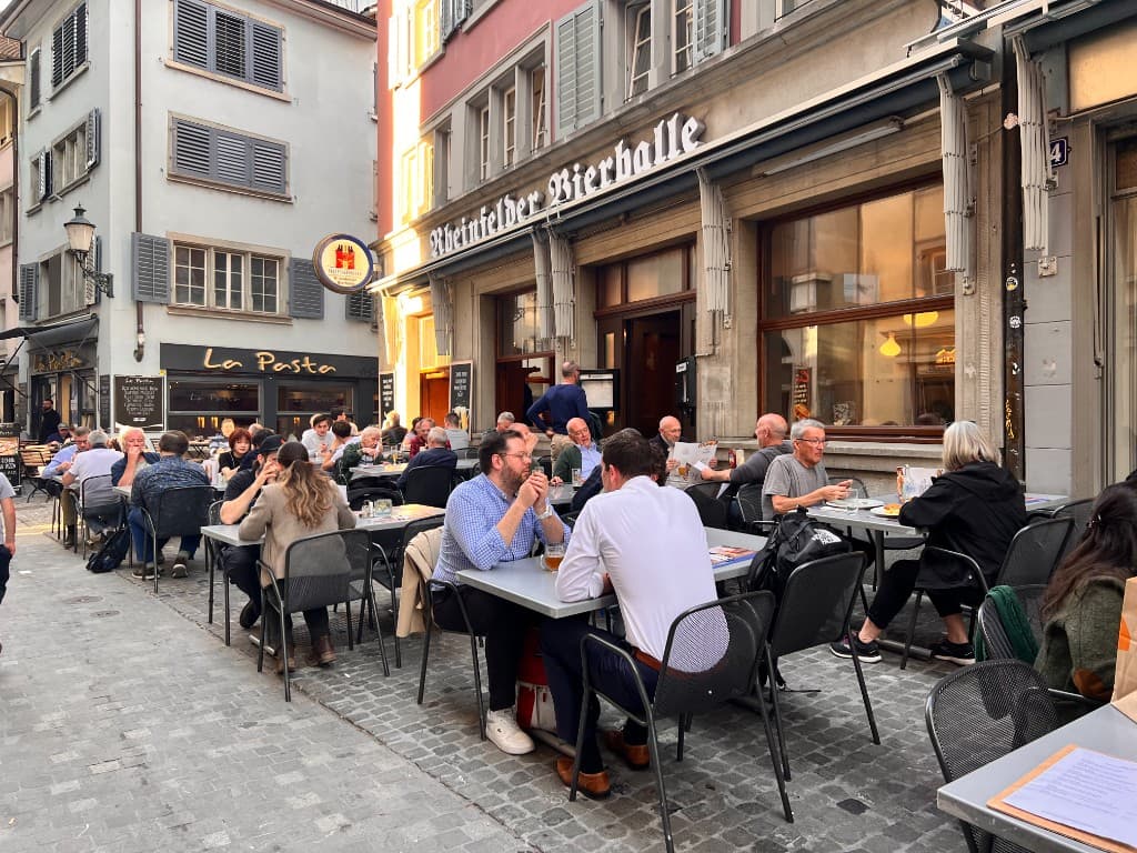 Historische Sepia-Aufnahme: Gruppe von Menschen vor der Rheinfelder Bierhalle mit Schriftzug am Gebäude, frühes 20. Jahrhundert.
